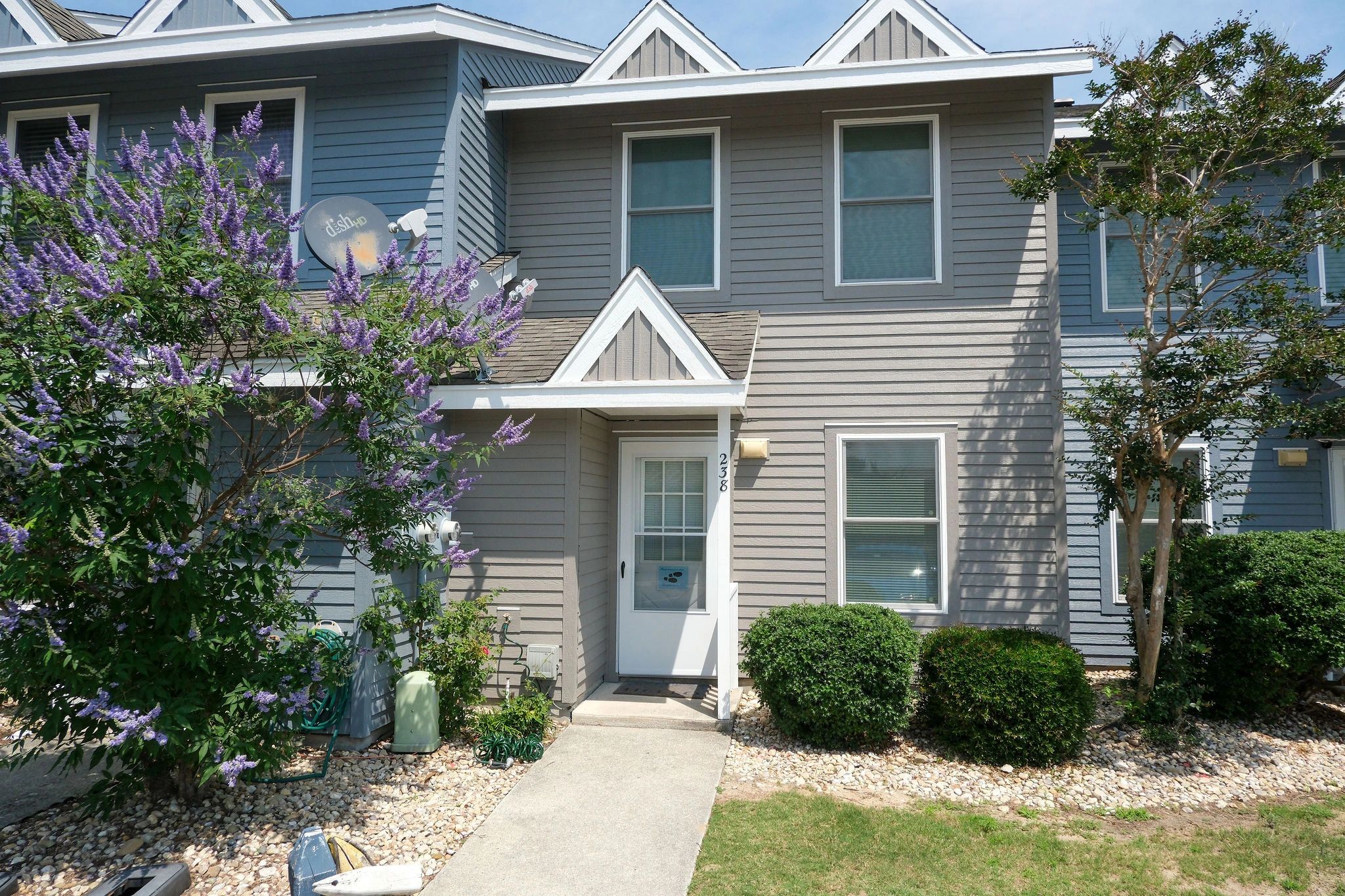 Gray townhouse with purple flowers and greenery.