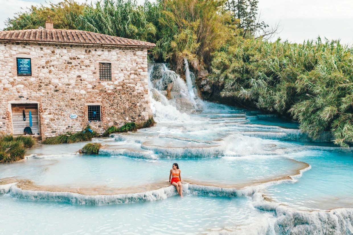 Woman sitting in blue water terraces near an old stone building.