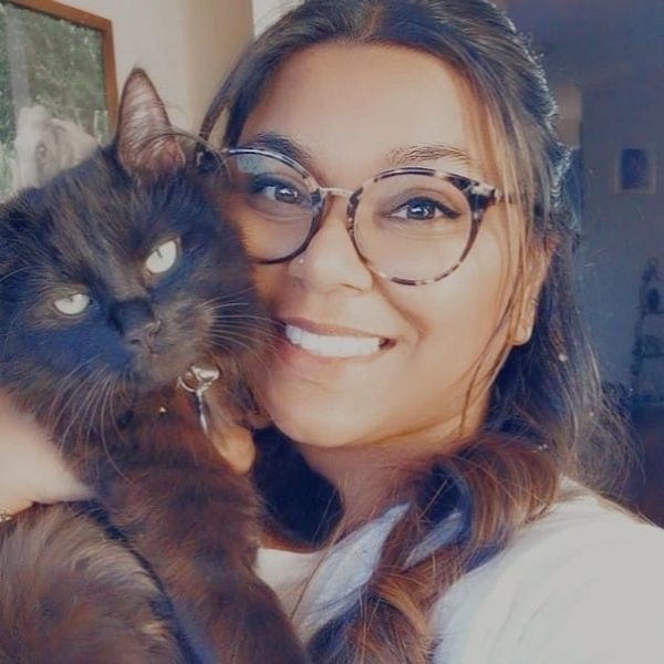 Woman with glasses smiling while holding a fluffy black cat.
