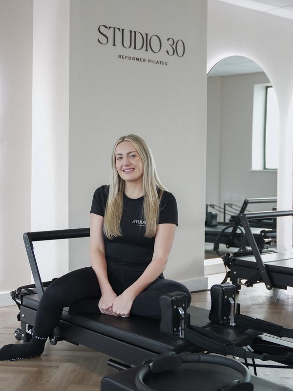 Woman in black activewear sitting on a Pilates reformer in Studio 30.