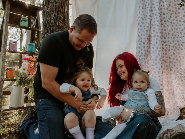 Johnnie, Ash and their two daughters smiling at the camera to showcase the family‑owned business