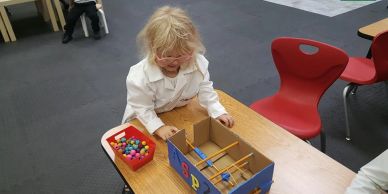 A child playing with a homemade pinball game at a classroom desk.
