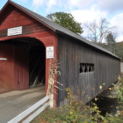 Red and black covered bridge over a stream in autumn.
