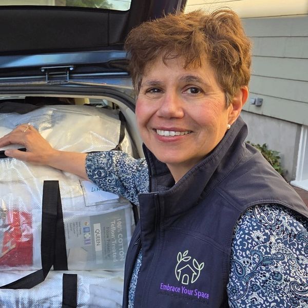 Smiling woman packing bags into a car, wearing an 'Embrace Your Space' vest.