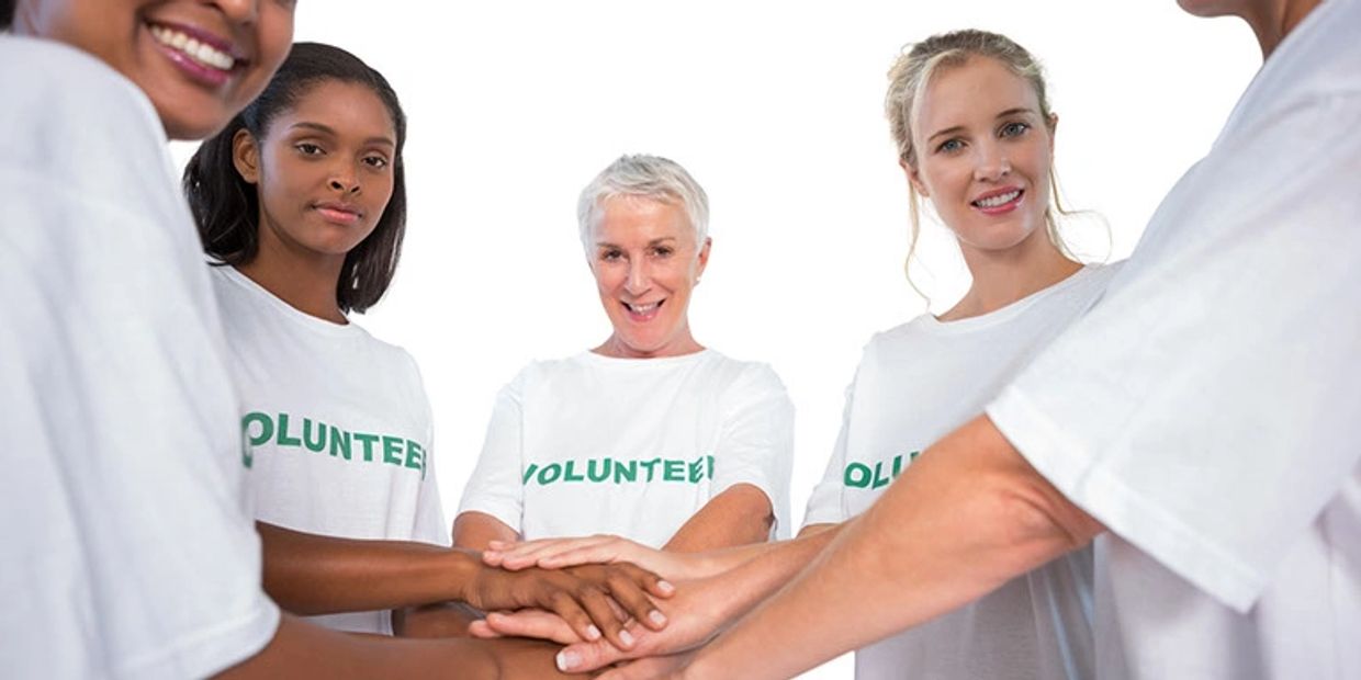 Picture of people in white t-shirts with the word "Volunteer" on the front holding hands in a circle