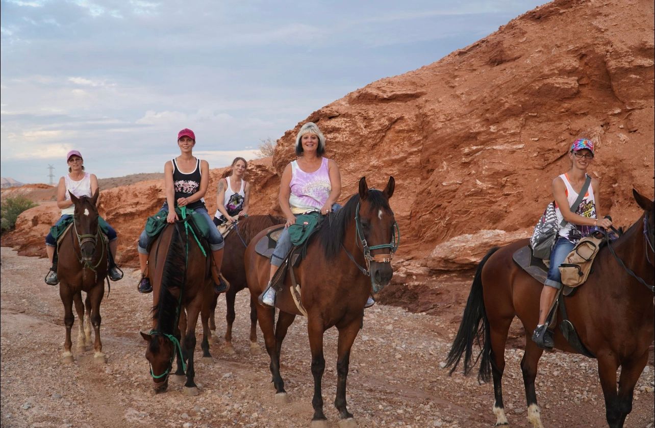 Five women horseback riding on a rocky desert trail.