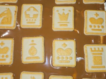 Cookies decorated with various crown and royal symbols on a caramel or toffee surface.