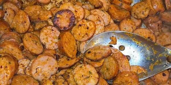Close-up of cooked sausage slices with a metal spoon.