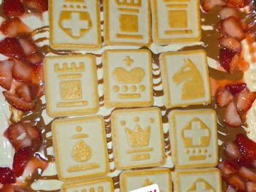 Chess-themed cookies surrounded by sliced strawberries and caramel drizzle.