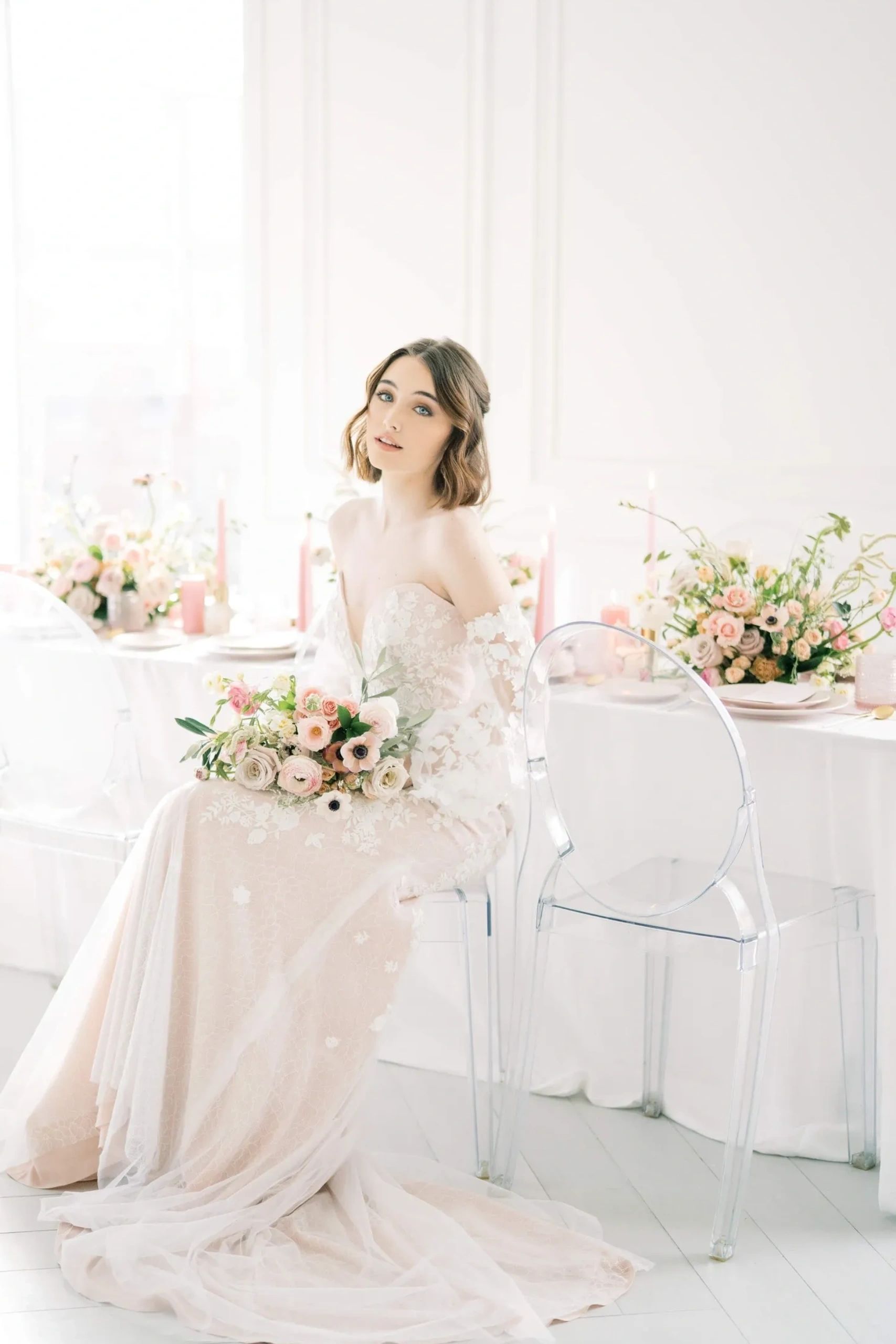 Bride in elegant white dress holding a bouquet, surrounded by greenery and candles.
