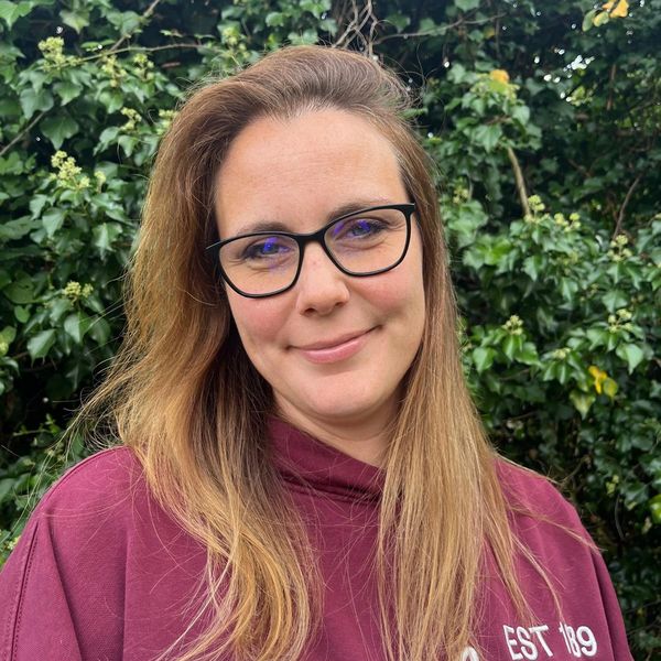 Woman with glasses smiling outdoors in a maroon hoodie.