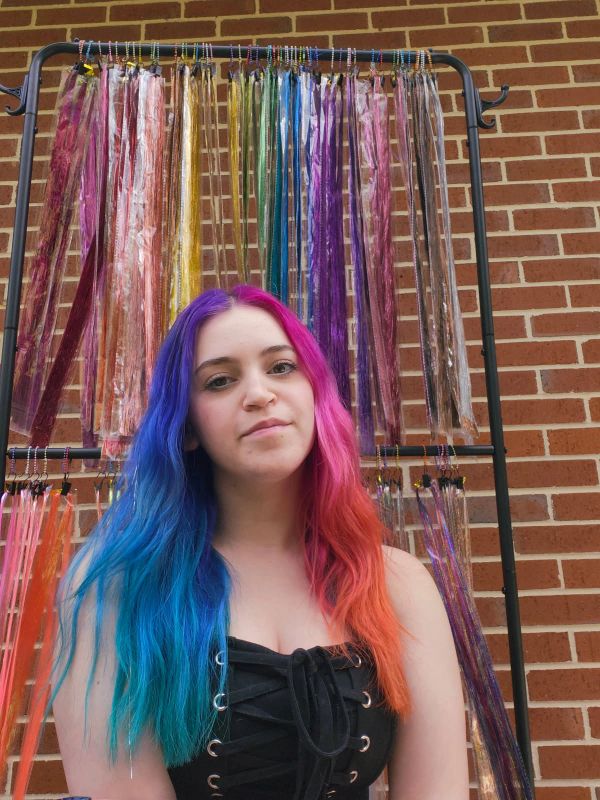 Woman with vibrant blue and pink hair in front of colorful accessories.