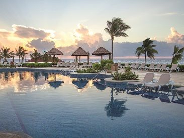 Sunset by a tropical pool with palm trees and lounge chairs.