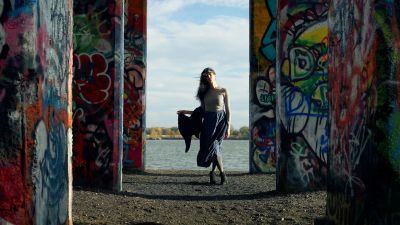 Woman walking through graffiti-covered pillars by the water.