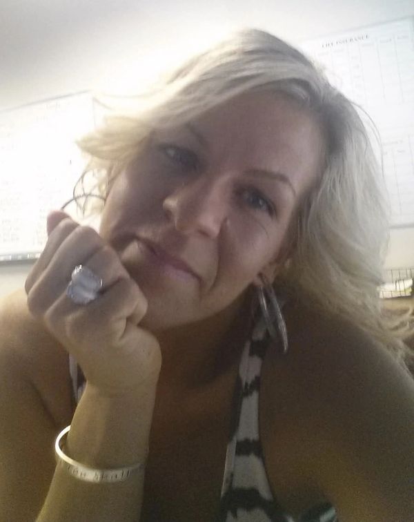 Woman with blonde hair resting her chin on her hand, wearing a ring and bracelet.