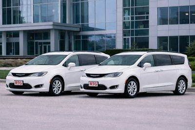 Two white minivans parked side by side in front of a modern building.