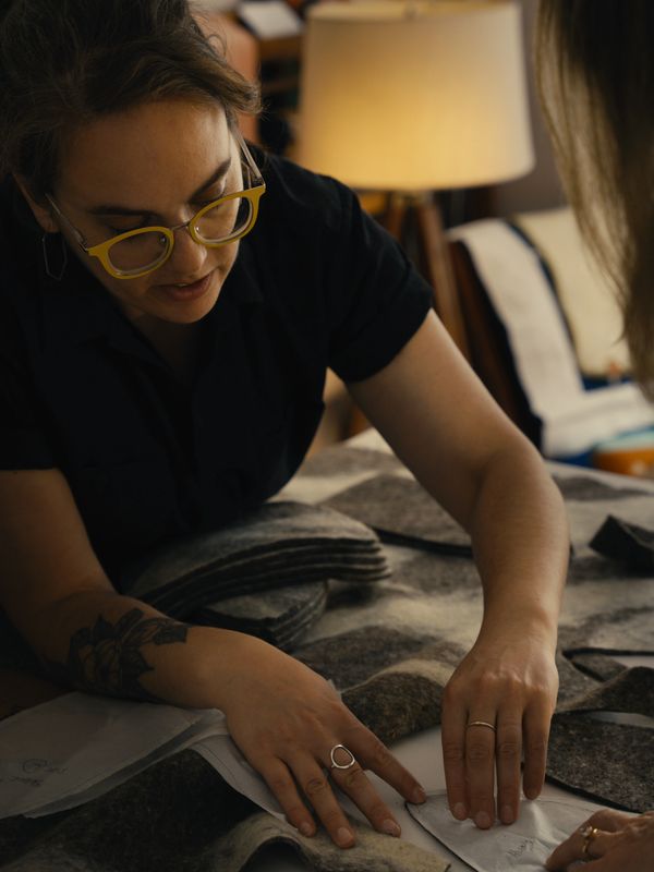 Rebecca leans over a table and points out a detail on a pattern piece