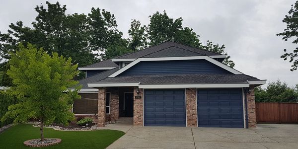 Exterior repaint of a blue house with white trim and stone work completed by Dean's Painting
