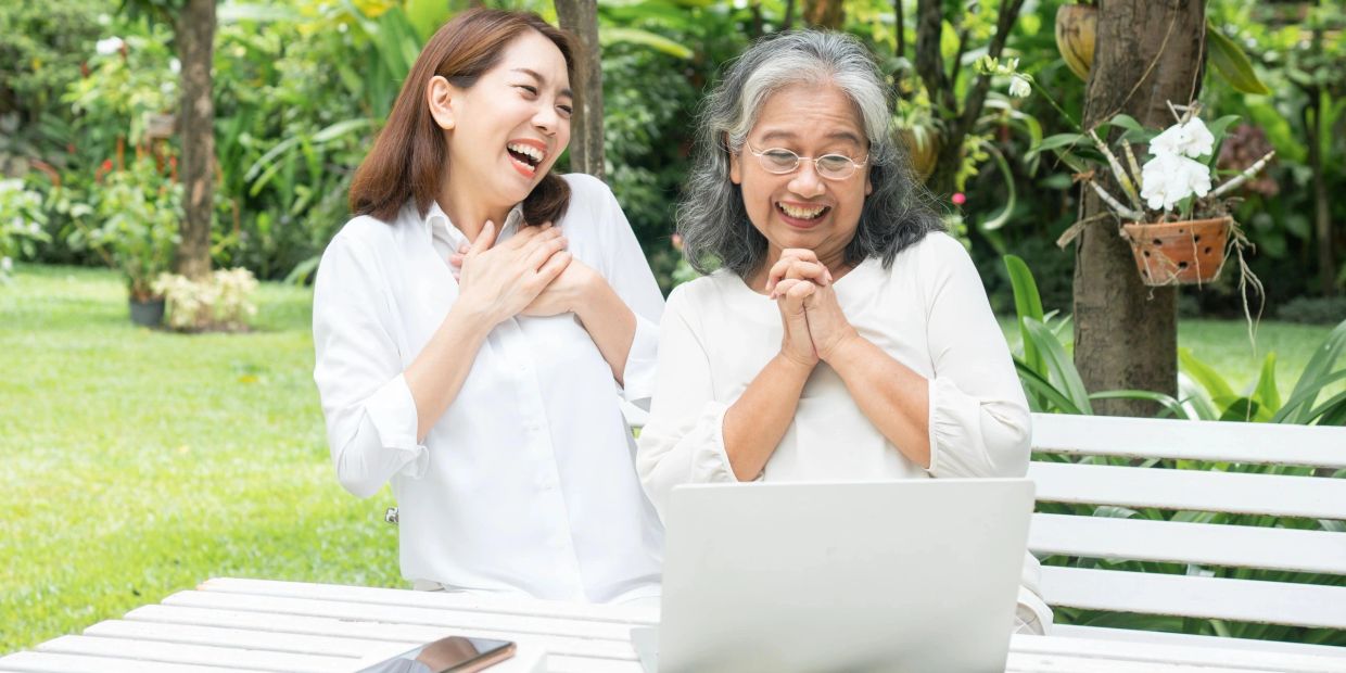 Two women happily looking at a laptop outdoors.