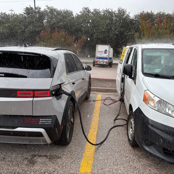 Electric car charging with a connected white van in rainy weather.