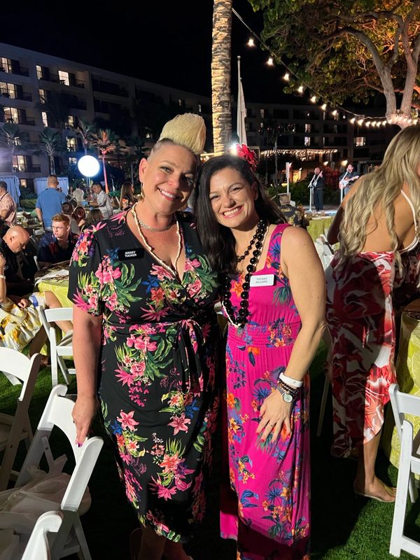 Two women in floral dresses smiling at a nighttime outdoor party.