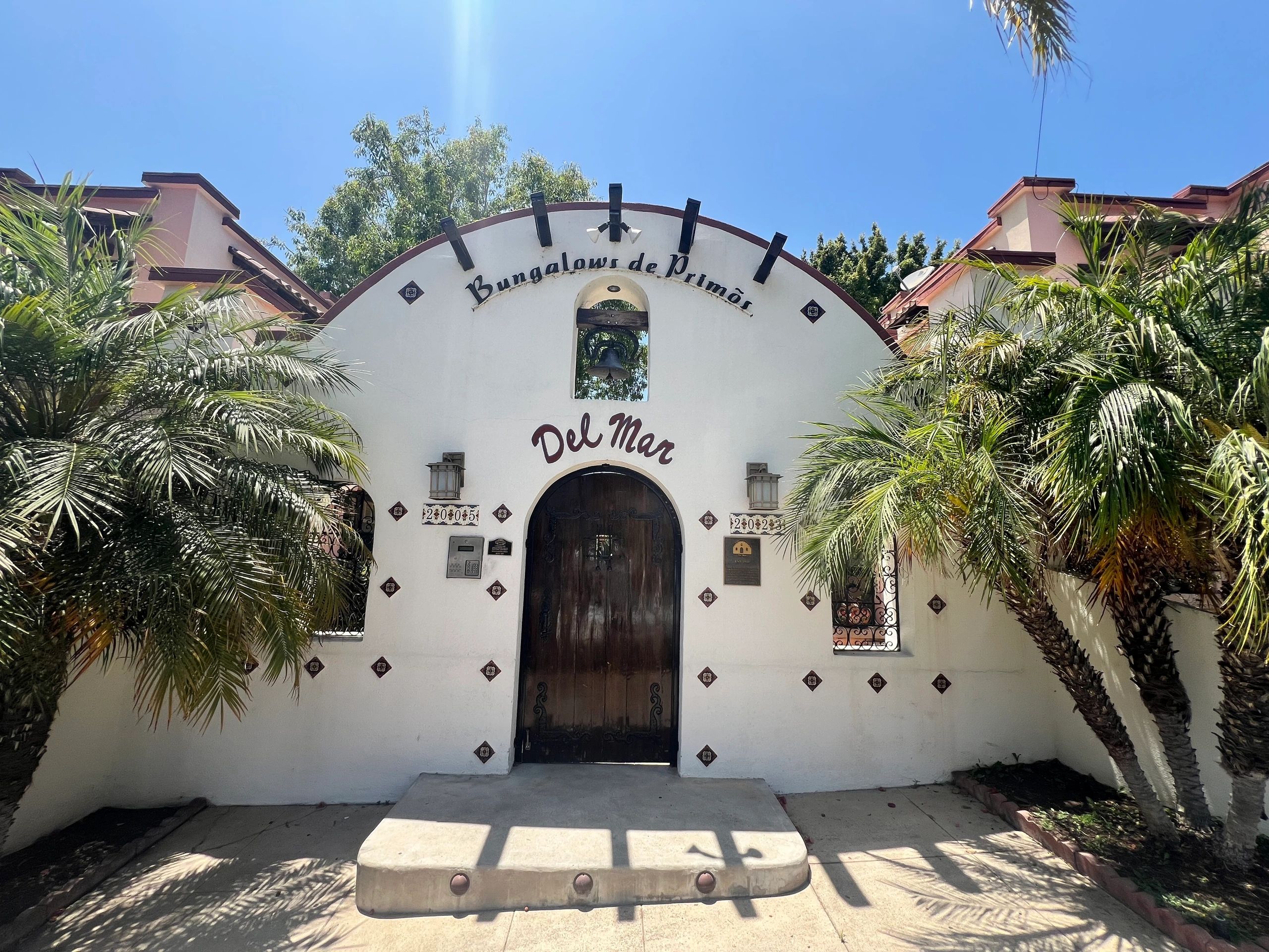 Entrance of Bungalows de Primôs Del Mar with palm trees and a clear blue sky.