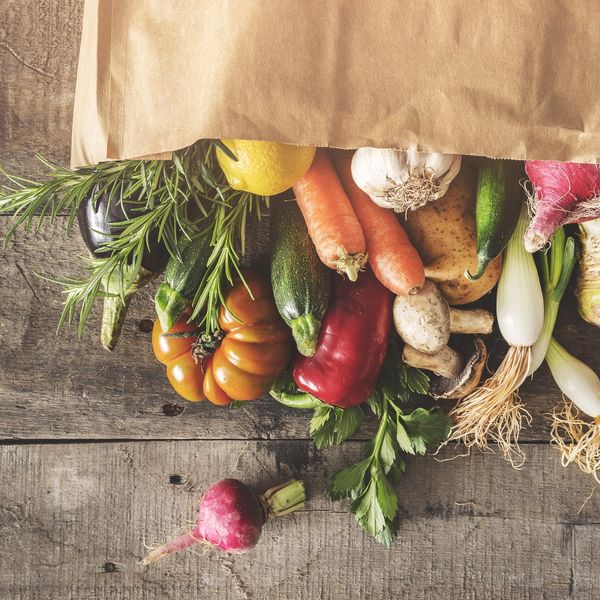 Fresh vegetables spilling out of a brown paper bag on a wooden surface.