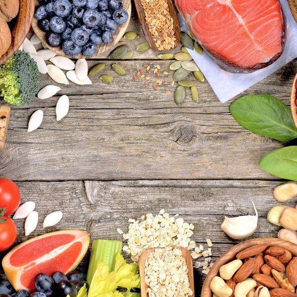 A variety of fresh fruits, nuts, seeds, and salmon arranged on a wooden surface.