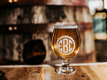 A picture of a tulip glass with the EBC logo with a beer sitting in front of a barrel.