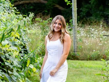 Young woman in a white dress smiling outdoors in a garden.