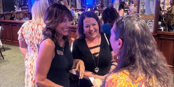 Three women laughing together indoors at a social event.