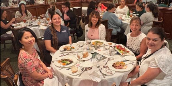 Five women seated around a dining table with plates of food.
