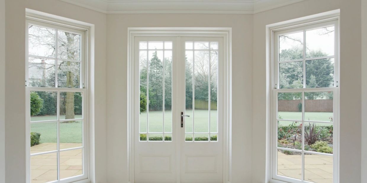 Bright room with white-framed windows and glass doors overlooking a green garden.