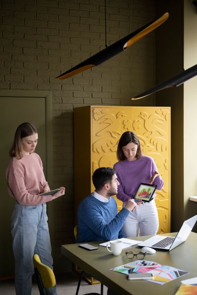Three colleagues collaborate in a modern office with digital devices and colorful decor.