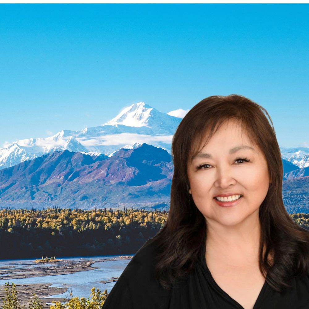 Smiling woman with snowy mountains and river in the background.