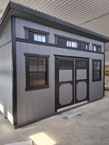 A gray and black wooden shed with multiple windows and double doors.