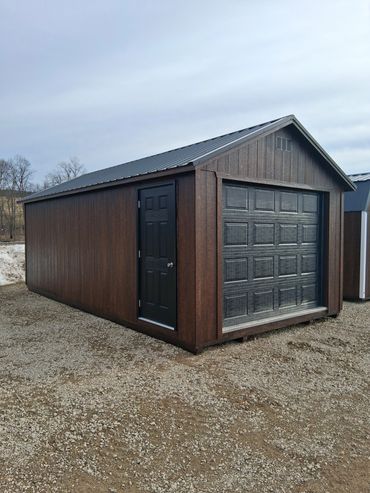Wooden garage with a black door and garage door on gravel.