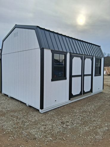 White and black storage shed with metal roof on gravel ground.