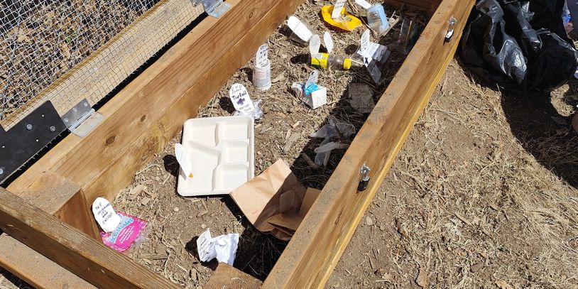 A garden bed with seed packets and a planting tray on dry soil.