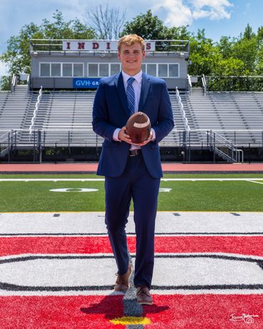 Young man in a blue suit holding a football on a sports field.