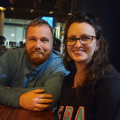 Smiling couple sitting at a wooden table in a cozy nighttime setting.
