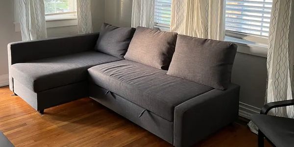 Modern gray sectional sofa in a sunlit living room with wooden floors and white curtains.