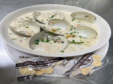 A bowl of clam chowder garnished with herbs and oyster crackers.