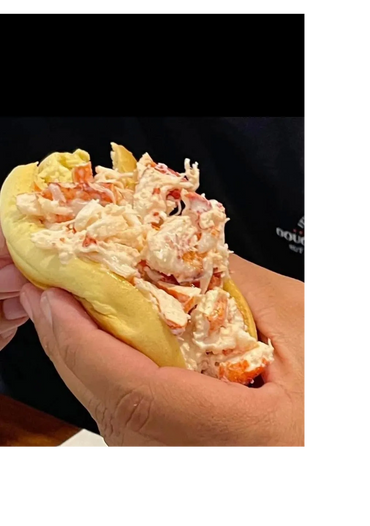 Hand holding a creamy lobster roll sandwich.