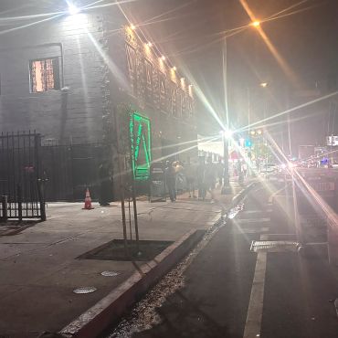 Nighttime street scene with bright lights and people gathered outside AcademyLA . We are right next door!