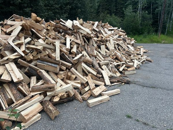 A large pile of chopped firewood stacked outdoors on pavement.