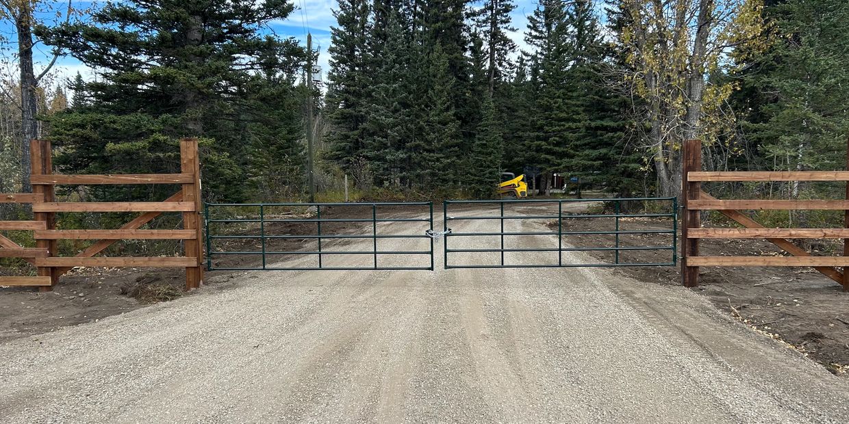 A gated gravel driveway leading into a forested area under a blue sky.