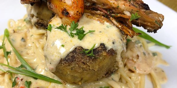 Creamy pasta topped with grilled shrimp and seasoned patties garnished with herbs.