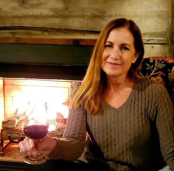 Woman enjoying a glass of red wine near a cozy fireplace.