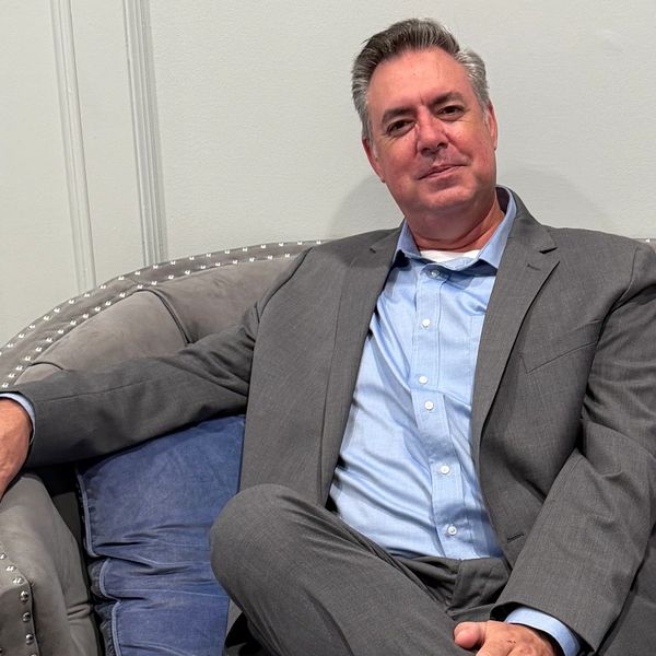 Man in a gray suit sitting on a gray couch.